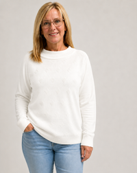 Woman wearing a white knit jumper  and blue jeans against a gray background