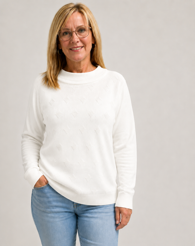 Woman wearing a white knit jumper  and blue jeans against a gray background