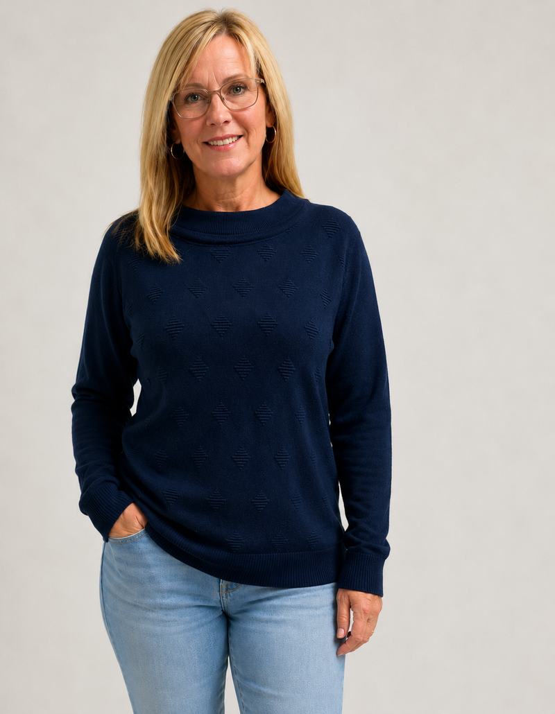 Woman wearing a navy sweater and light blue jeans against a plain background