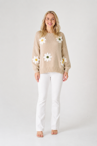 Woman wearing a beige knit jumper with floral patterns and white pants.