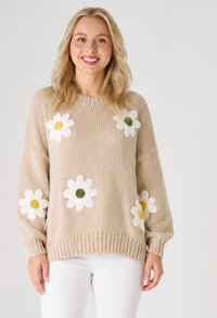 Woman wearing a beige knit jumperwith white daisy flowers on a plain background