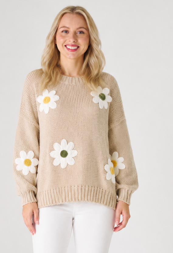 Woman wearing a beige knit jumperwith white daisy flowers on a plain background
