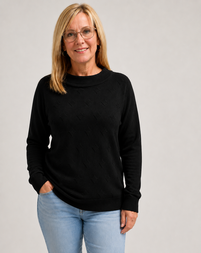 Woman wearing a black knit jumper and light blue jeans on a gray background