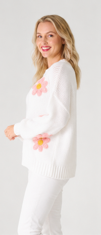 Woman wearing a white knit jumper  with pink flower designs on a plain background