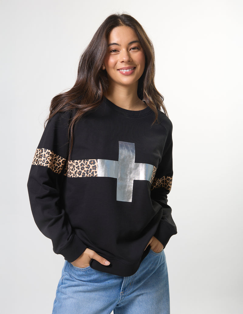 Woman wearing a black sweater with leopard print and silver cross design on a white background