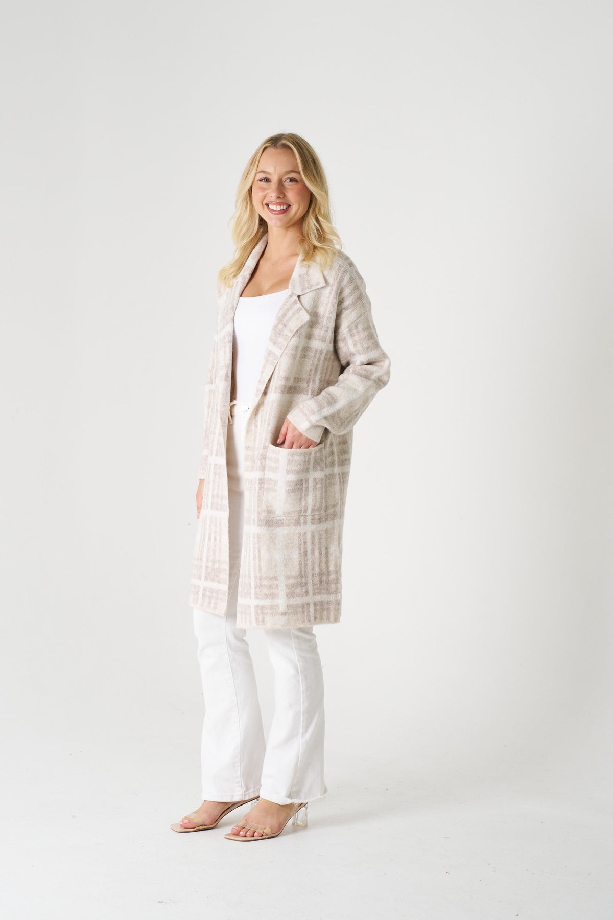 Woman wearing a long plaid coat over a white top and pants on a white background