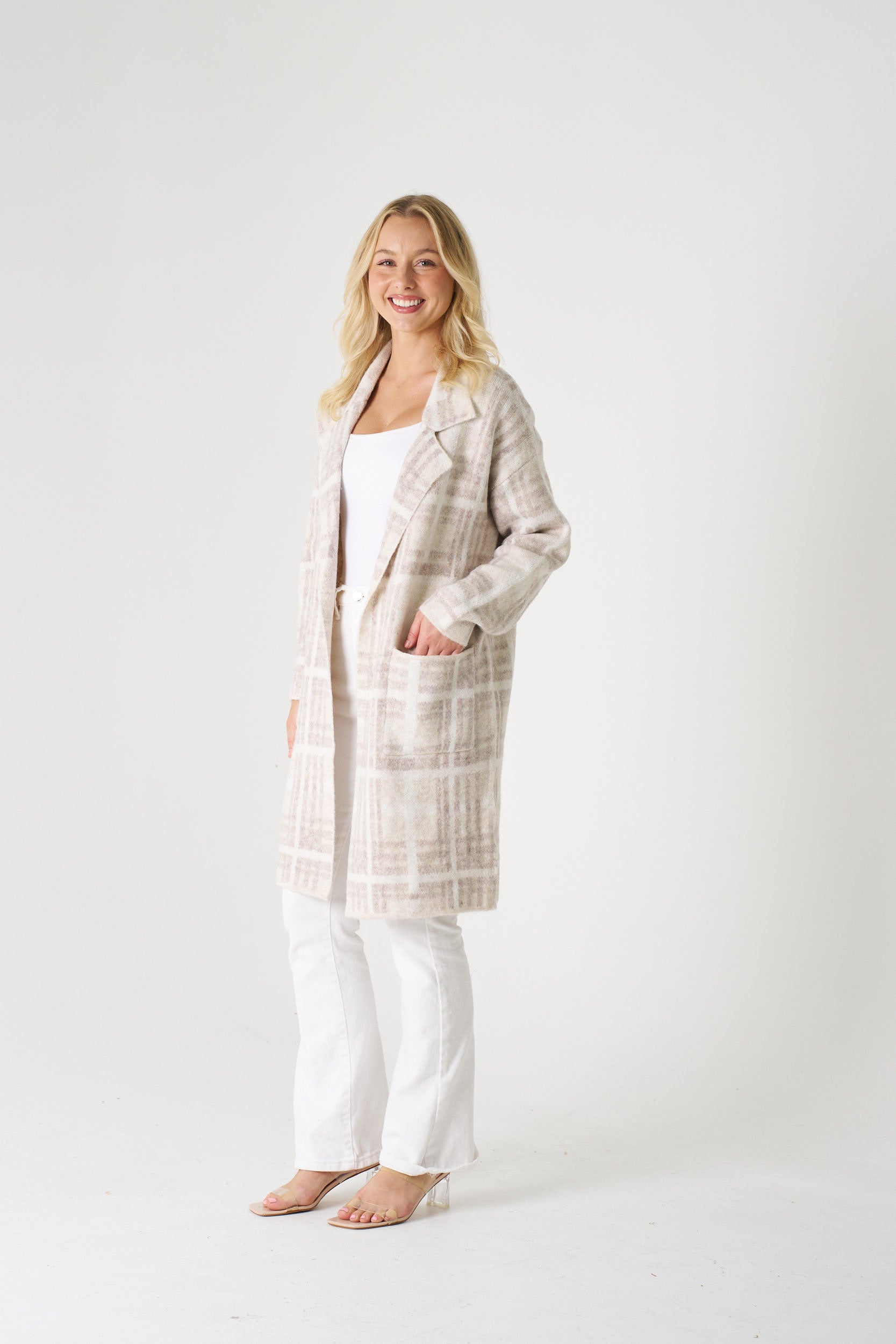 Woman wearing a long plaid coat over a white top and pants on a white background