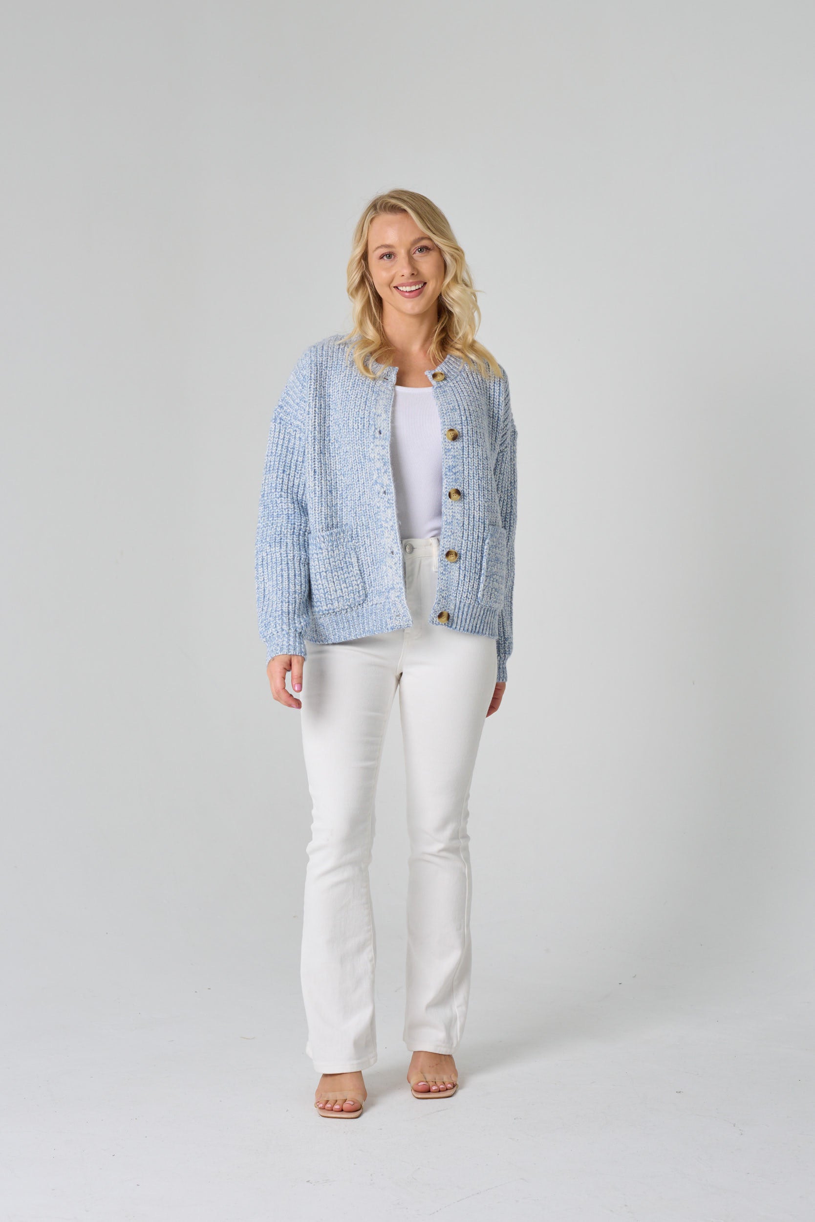 Woman wearing a light blue textured cardigan over a white top and pants on a plain background