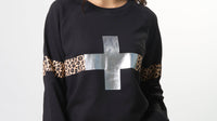 Woman wearing a black sweater with leopard print and silver cross design on a white background