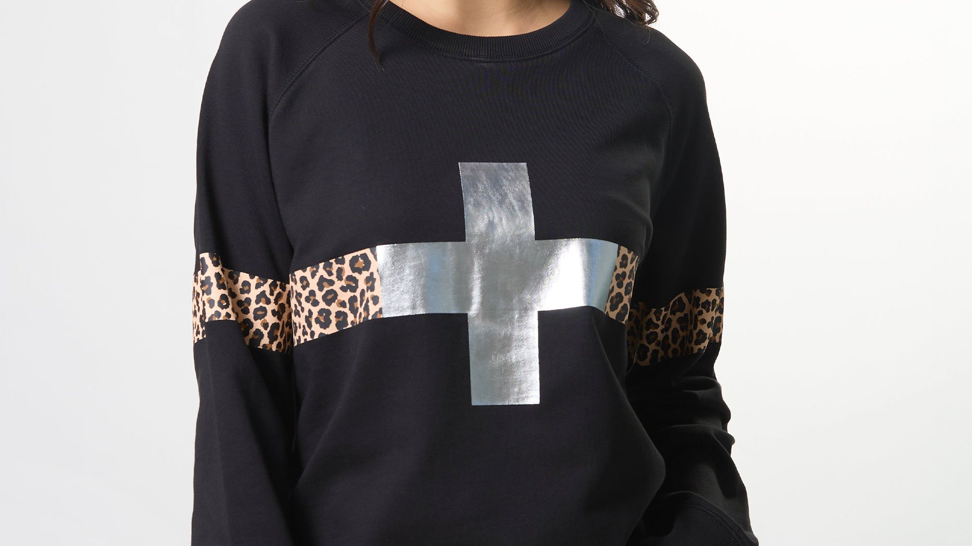 Woman wearing a black sweater with leopard print and silver cross design on a white background