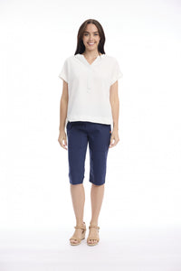 A woman modeling a white short-sleeve collared top and navy blue cropped pants with beige sandals, standing against a plain white studio background.