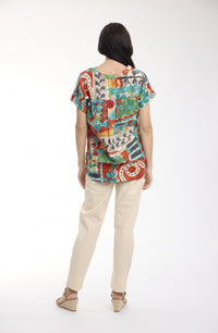 A woman viewed from the back wearing a colorful short-sleeve top with an abstract multicolor print, paired with light beige pants and beige wedge sandals, against a plain white studio background.